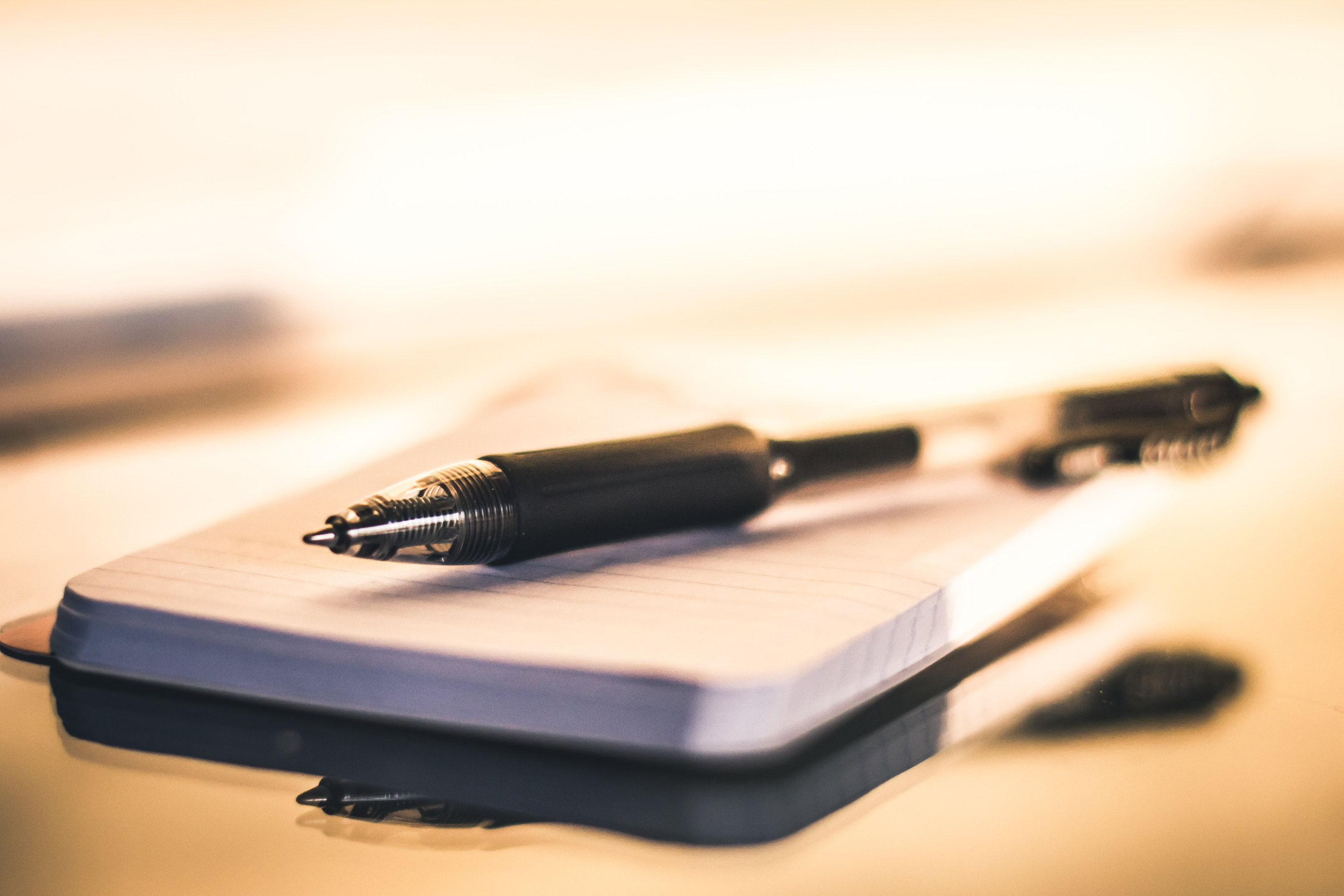 A notebook and pens on a desk in warm light