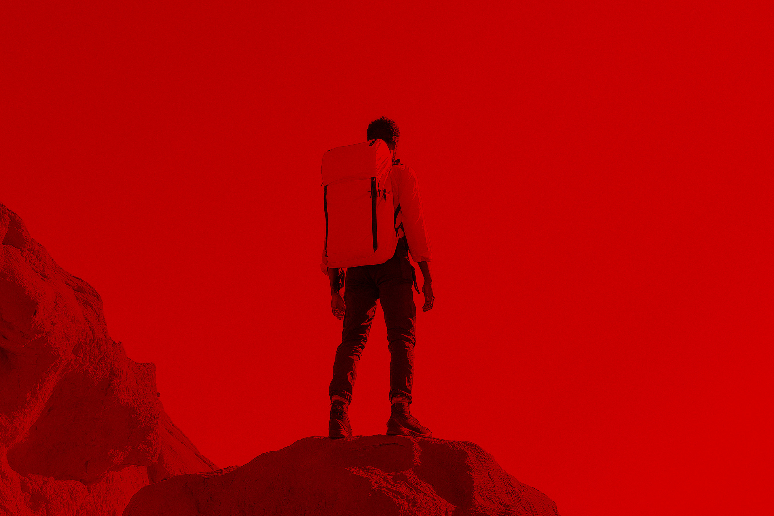 A figure standing on a peak against a deep red sky